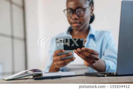 Making online payment, holding credit card. Woman is at home in domestic room Making online payment, holding credit card. Woman is at home in domestic room 135834412