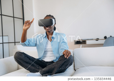 On the sofa in virtual reality headset. Woman is at home in domestic room On the sofa in virtual reality headset. Woman is at home in domestic room 135834446