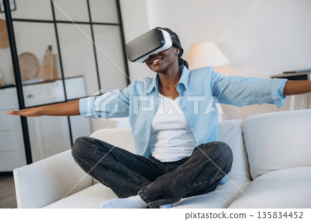 Playing game of flying, in VR glasses. Woman is at home in domestic room Playing game of flying, in VR glasses. Woman is at home in domestic room 135834452