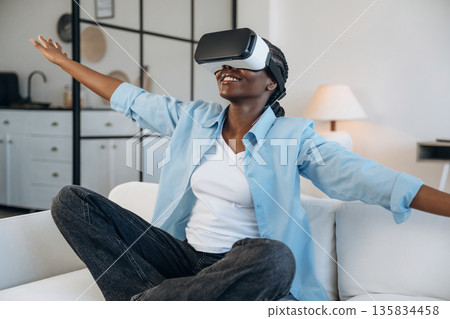 Augmented reality headset, sitting on sofa. Woman is at home in domestic room 135834458