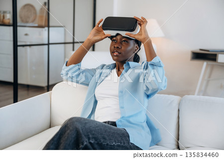 Augmented reality headset, sitting on sofa. Woman is at home in domestic room 135834460