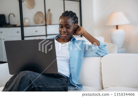 Working by using laptop, sitting on sofa. Woman is at home in domestic room Working by using laptop, sitting on sofa. Woman is at home in domestic room 135834466