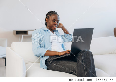 Working by using laptop, sitting on sofa. Woman is at home in domestic room Working by using laptop, sitting on sofa. Woman is at home in domestic room 135834467