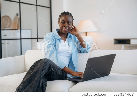 Working by using laptop, sitting on sofa. Woman is at home in domestic room Working by using laptop, sitting on sofa. Woman is at home in domestic room 135834468