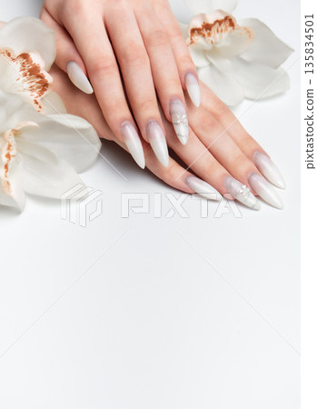 Elegant hands displaying long white almond nails with orchid flowers Elegant hands displaying long white almond nails with orchid flowers 135834501