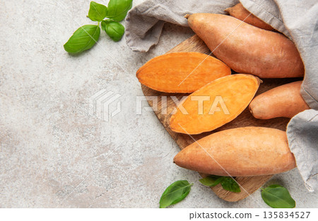 Sweet potatoes on cutting board with basil leaves Sweet potatoes on cutting board with basil leaves 135834527