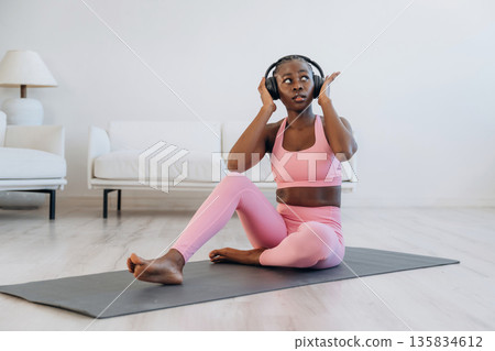 Listening to the music in headphones. Woman is doing yoga at home Listening to the music in headphones. Woman is doing yoga at home 135834612