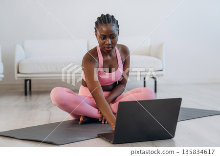 Taking online lessons by using laptop. Woman is doing yoga at home Taking online lessons by using laptop. Woman is doing yoga at home 135834617