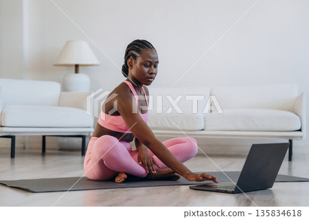 Taking online lessons by using laptop. Woman is doing yoga at home 135834618
