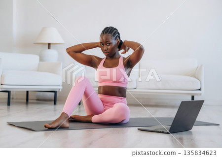 On the yoga mat, sitting, laptop on floor. Woman is doing yoga at home 135834623