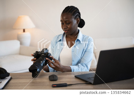 Professional camera in hands. Woman is at home in domestic room Professional camera in hands. Woman is at home in domestic room 135834662