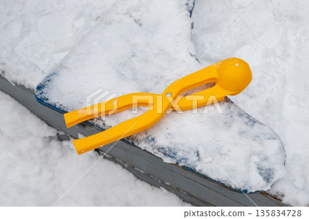 Yellow snowball maker on snowy surface. Winter fun and outdoor play tool for kids. Plastic equipment for making snowballs. Yellow snowball maker on snowy surface. Winter fun and outdoor play tool for kids. Plastic equipment for making snowballs. 135834728
