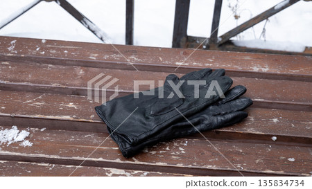 pair of black leather gloves on weathered wooden bench with snow. Winter accessory for cold weather protection and style. 135834734