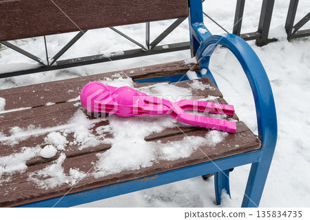 Magenta pink snowball maker on snowy bench. Winter fun and outdoor play tool for kids. Plastic equipment for making snowballs. 135834735