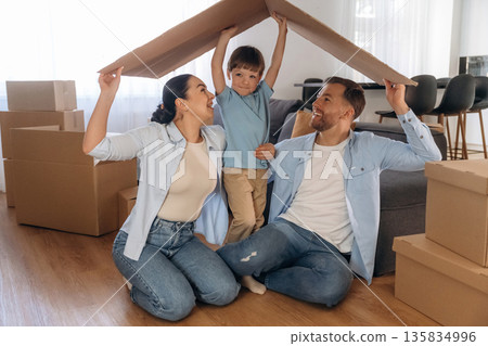 Front view, holding paper from box, sitting. Family of husband, wife and son are moving into new house Front view, holding paper from box, sitting. Family of husband, wife and son are moving into new house 135834996