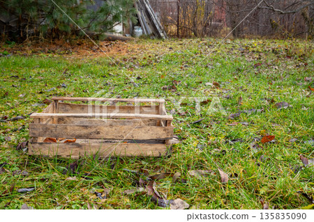 Empty rustic wooden crate on green grass in garden. Simple box for collecting harvest or as decorative element in outdoor setting. 135835090