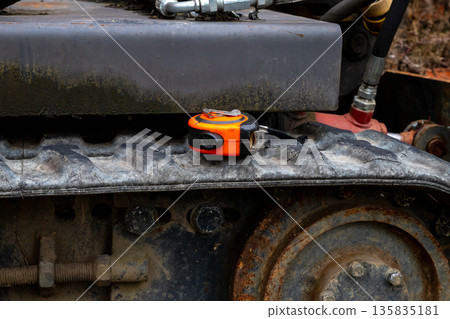 Construction measuring tape on a tractor track. Construction work, heavy equipment maintenance, and agricultural machinery repair concept for industry. Construction measuring tape on a tractor track. Construction work, heavy equipment maintenance, and agricultural machinery repair concept for industry. 135835181