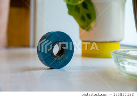 Roll of blue electrical tape on a white surface, with a plant pot in the background. Tool for repair and DIY projects. 135835188