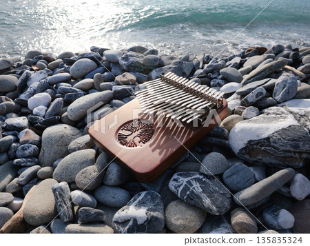 Kalimba musical instrument on stones by sea. Nature near mountains, music, and meditation. Relaxation and mental health. Kalimba musical instrument on stones by sea. Nature near mountains, music, and meditation. Relaxation and mental health. 135835324