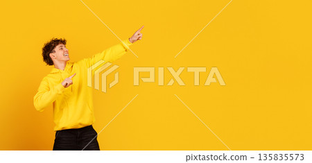 Cheerful teenage guy pointing aside at copy space on yellow studio background 135835573