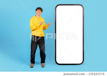 Teenage boy pointing at large smartphone with empty screen on blue background 135835574