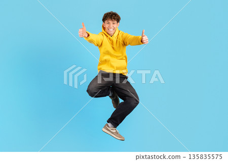 Young man jumping with both thumbs up on blue studio background 135835575