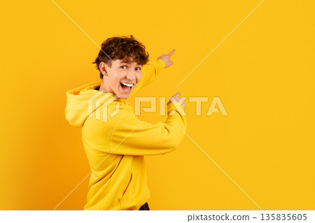 Excited teen boy pointing backward with open mouth smile on studio background 135835605