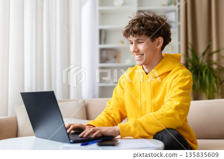 Smiling young man working on laptop at home, casual remote work lifestyle 135835609