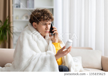 Sick man sitting on sofa, talking on smartphone and holding medicine bottle Sick man sitting on sofa, talking on smartphone and holding medicine bottle 135835623