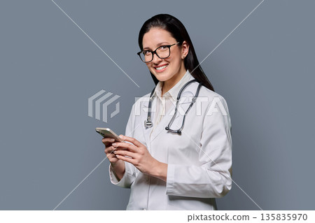 Middle aged female doctor holding smartphone, on grey studio background 135835970