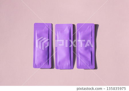 Three purple cosmetic sachet packets on light pink background. 135835975