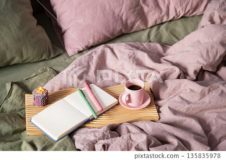 Open notebook and coffee cup on wooden tray with lit candle. 135835978