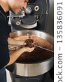Cheerful male employee holding cooled roasted beans above machine drum and checking the quality  135836091