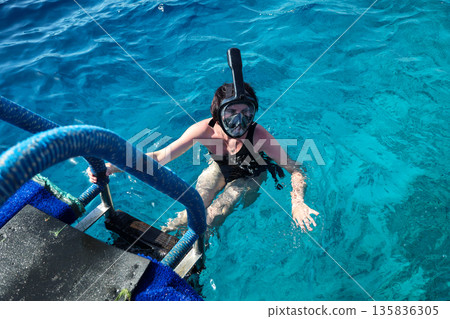 A woman overcomes her fear as she puts on a snorkel mask for the first time and dives into the water A woman overcomes her fear as she puts on a snorkel mask for the first time and dives into the water 135836305