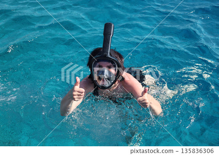 A woman overcomes her fear as she puts on a snorkel mask for the first time and dives into the water A woman overcomes her fear as she puts on a snorkel mask for the first time and dives into the water 135836306