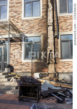 Charred vertical strip on brick wall marks fire path; broken window, scorched cabinet, and tangled wires lie amid debris in damaged urban setting. 135836630