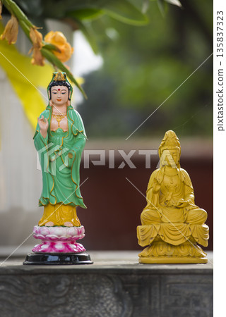 Two statues of Buddha, one green and one yellow, sit on a stone ledge Two statues of Buddha, one green and one yellow, sit on a stone ledge 135837323