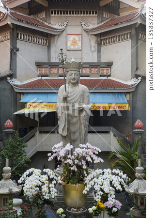 Statue of a Buddha figure is surrounded by flowers and plants Statue of a Buddha figure is surrounded by flowers and plants 135837327