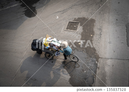 Man is riding a bicycle with a cart full of trash Man is riding a bicycle with a cart full of trash 135837328