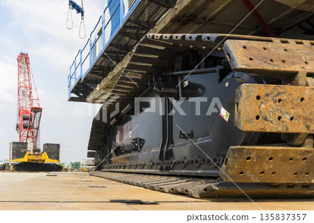 Large black and red construction vehicle with a crane in the background 135837357