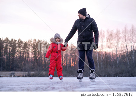 Father holding daughter hand while ice skating together on a frozen lake at sunset, winter family activity, bonding, care and outdoor leisure Father holding daughter hand while ice skating together on a frozen lake at sunset, winter family activity, bonding, care and outdoor leisure 135837612
