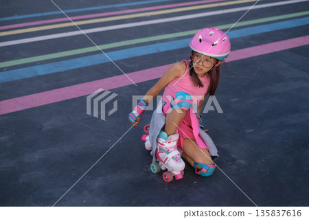 Young child practicing roller skating on an outdoor urban track while wearing helmet and protective pads. Concept of learning, safety, balance and active childhood with copy space. Young child practicing roller skating on an outdoor urban track while wearing helmet and protective pads. Concept of learning, safety, balance and active childhood with copy space. 135837616