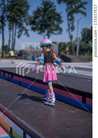 Child mastering roller skating on a skate park ramp while wearing protective equipment, focusing on coordination, control and safe movement during practice. 135837617