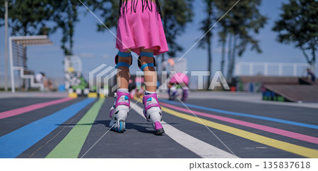 Child wearing protective gear roller skating at an outdoor skate park. Active childhood, learning balance, movement and coordination, summer sports activity with safety equipment. Child wearing protective gear roller skating at an outdoor skate park. Active childhood, learning balance, movement and coordination, summer sports activity with safety equipment. 135837618
