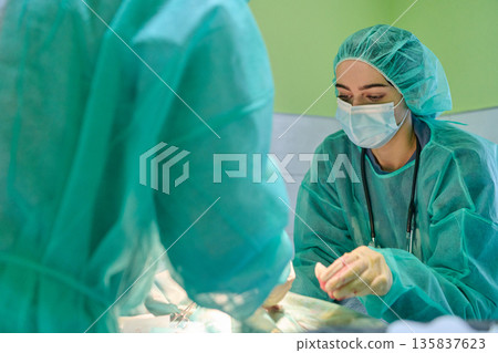 Surgeon And Nurse In Green Scrubs Performing Surgery In Operating Room During Aseptic Procedure Surgeon And Nurse In Green Scrubs Performing Surgery In Operating Room During Aseptic Procedure 135837623