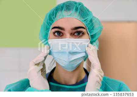 Healthcare Worker Putting On Surgical Mask With Gloves And Cap In Clinical Setting 135837653