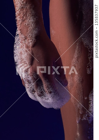 Close-up of a soapy hand on wet skin with soap bubbles against a dark blue background 135837937