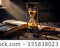 Hourglass measuring time beside old book and beads in historical interior 135838023
