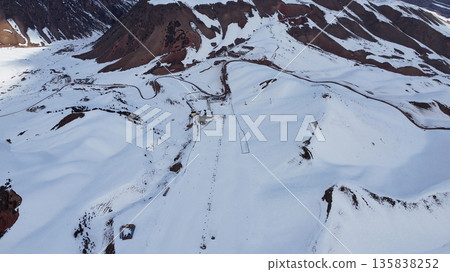 Aerial view of a snowy mountain ski resort. Winter landscape with slopes, chairlifts, and buildings for ski trip concept. 135838252