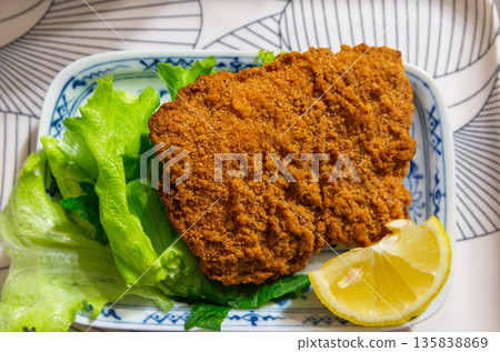 Crispy large chicken cutlet served with lettuce and lemon 135838869